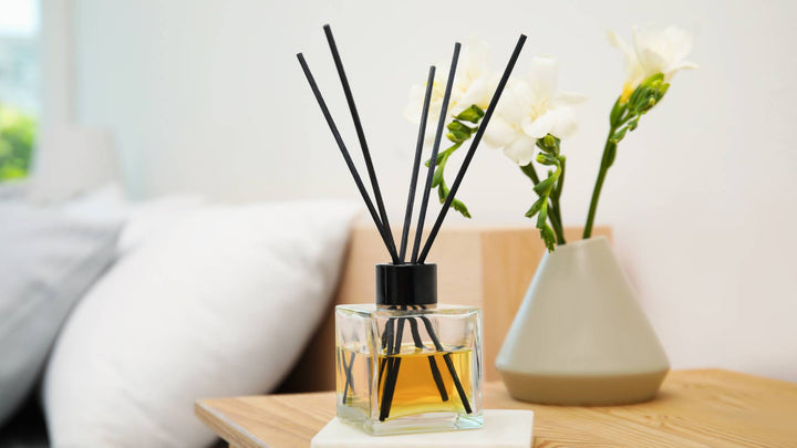 A modern reed diffuser on a side table, complete with five black reeds sticking out from a glass container of essential oils.